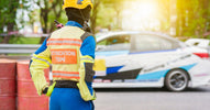 A person wearing a radio on their shoulder and high-vis clothing that says "EXTRICATION TEAM" on the back stands by a race car.