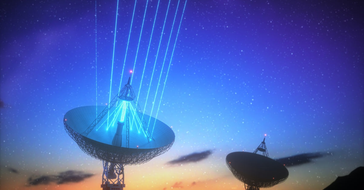 A large satellite dish beams blue signals into the sky at sunset. Another satellite nearby points in a different direction.